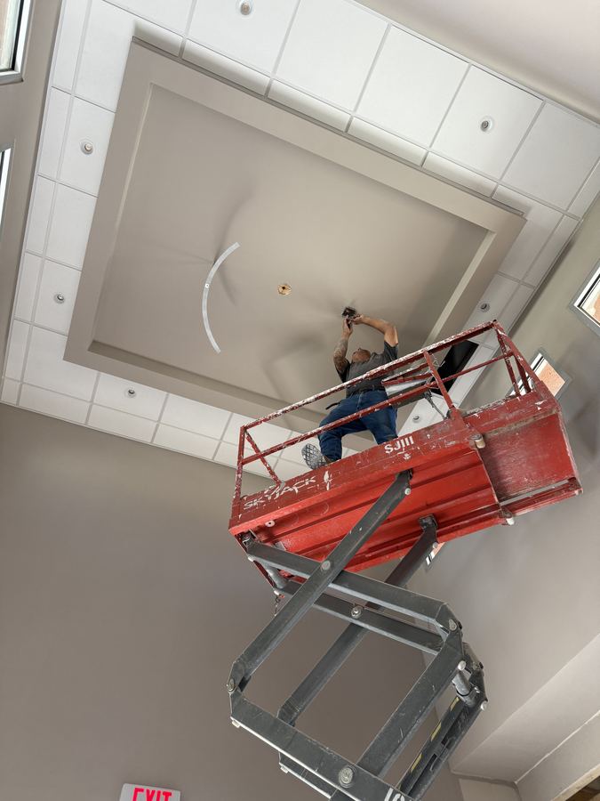Electrician on a scissor lift performing overhead finish work indoors
